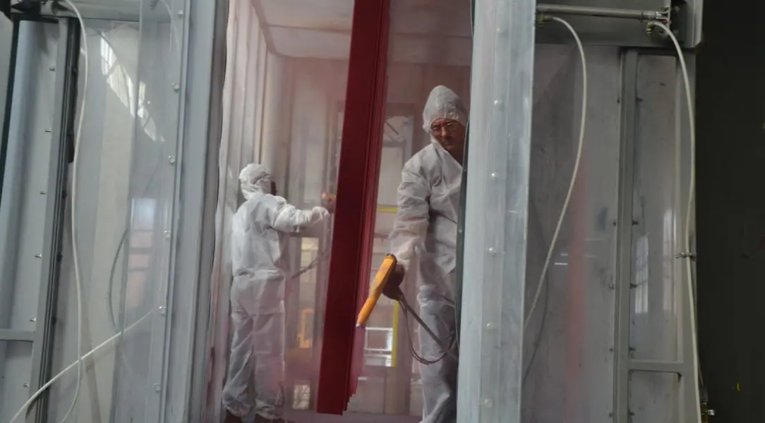 Two people in white suits spray painting a building.